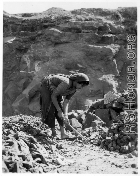 Woman crushes rock by hand, for use in construction.  Scenes in India witnessed by American GIs during WWII. For many Americans of that era, with their limited experience traveling, the everyday sights and sounds overseas were new, intriguing, and photo worthy.
