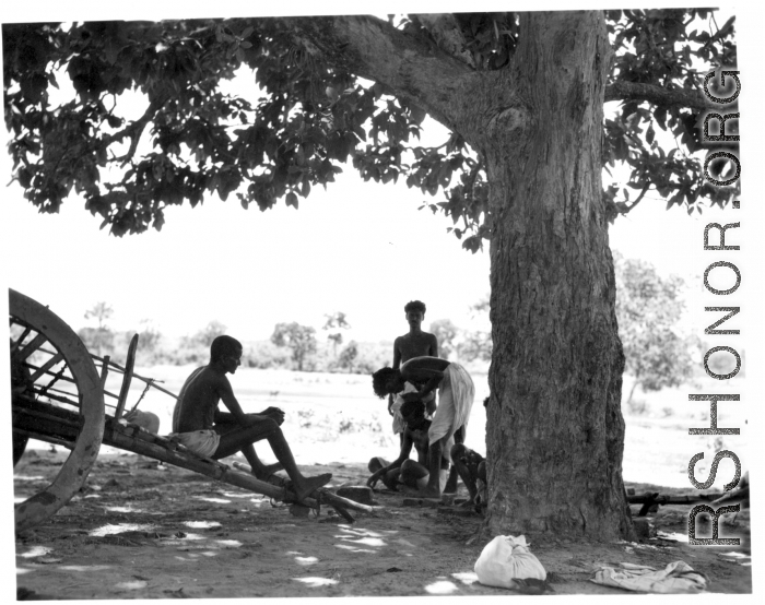 Man undergoes country haircut under tree.  Scenes in India witnessed by American GIs during WWII. For many Americans of that era, with their limited experience traveling, the everyday sights and sounds overseas were new, intriguing, and photo worthy.