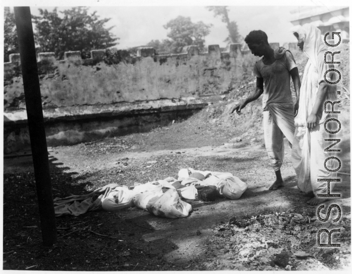 Men look at unfortunate souls, dead from famine, disease, or some other cause.  Scenes in India witnessed by American GIs during WWII. For many Americans of that era, with their limited experience traveling, the everyday sights and sounds overseas were new, intriguing, and photo worthy.