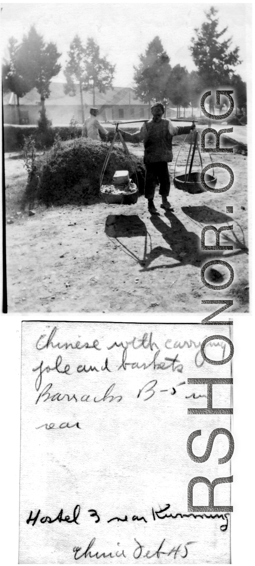 Daily life at Hostel #3, Kunming, China, on a day in February, 1945--Chinese worker carries item on shoulder pole, with barracks B-5 in the background.