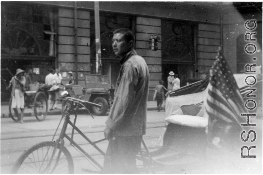Pedal-taxi driver with American flag. Probably after the end of war, in a large city like Shanghai.