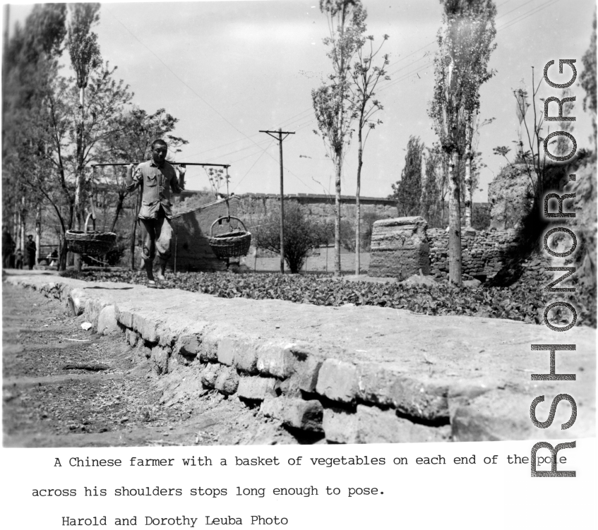 A farmer in northern China with baskets on a shoulder pole. Note the old town wall in the background.  Photo from Dorothy Yuen Leuba.