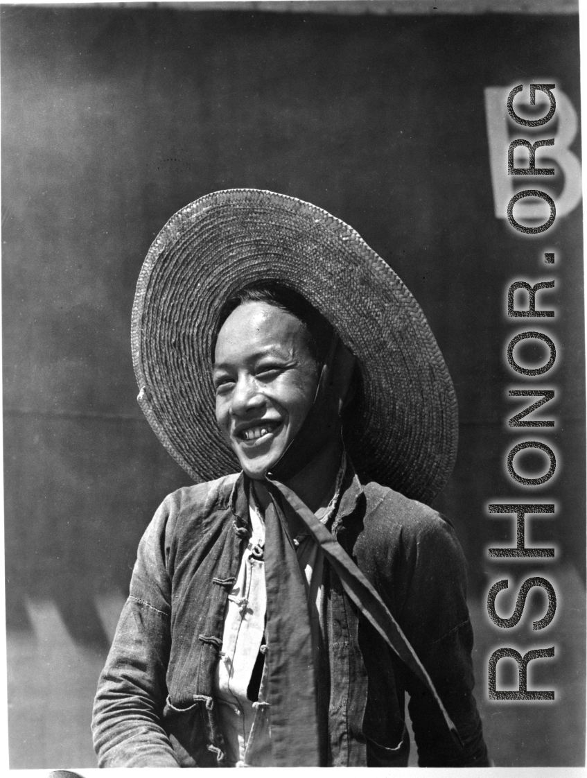 Local people in China: A smiling man stands in front of a large fuel tank.  From the collection of Eugene T. Wozniak.