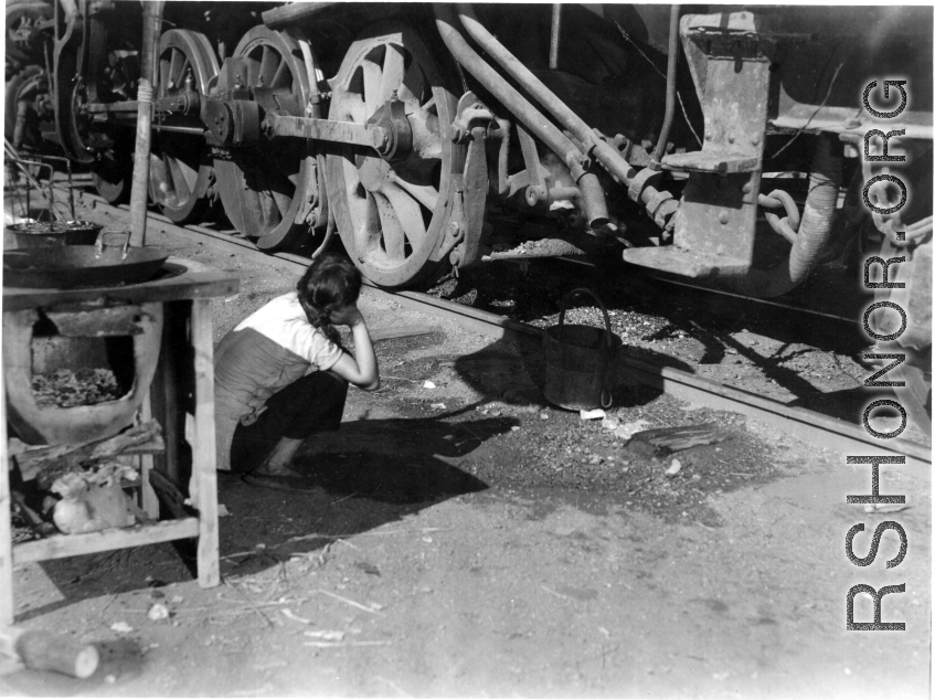 Chinese refugee waits with a bucket for hot water to drip from a steam train engine at the train station in Liuzhou during WWII, in the fall of 1944, as the Japanese advanced during the Ichigo campaign.