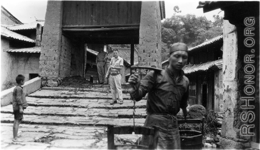 GIs go through village in Yunnan province, probably Yangkai village, carbines over shoulder, while local people go about their regular business. During WWII.