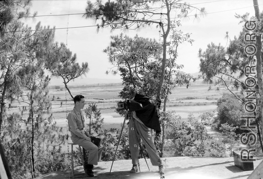 A photographer takes a portrait photo of an American serviceman. Yangkai valley in the background. During WWII in SW China. 