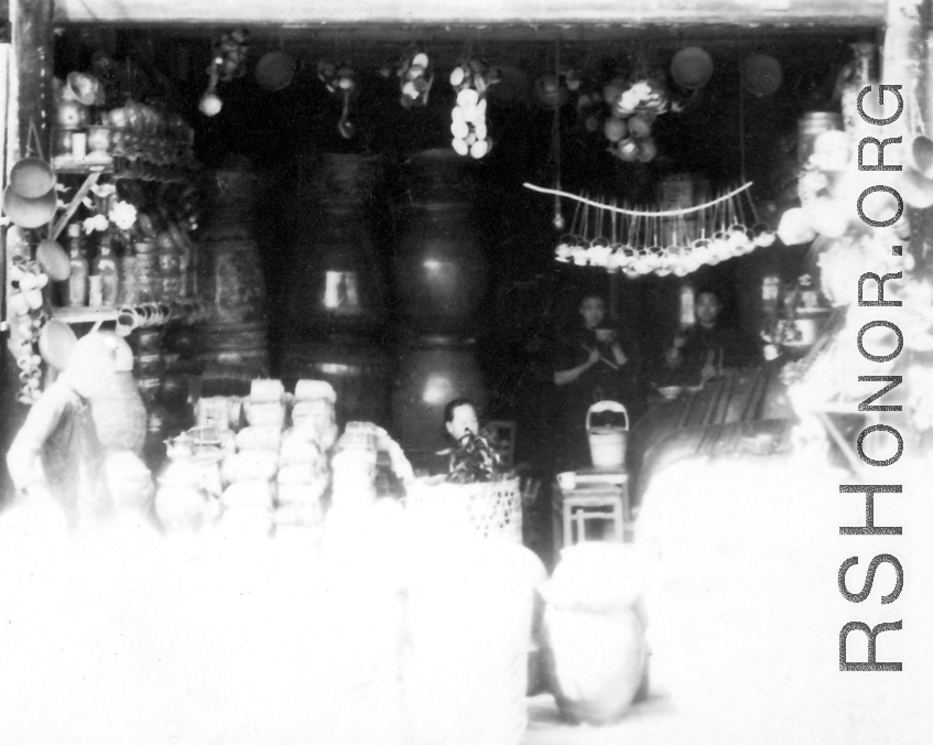 People holding bowls and chopsticks having lunch in a streetside shop selling cups, clay jars, cisterns, etc. SW China.  During WWII.