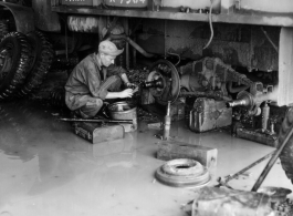 An American GI repairs a transport truck of the 14th Air Force in China, working in rough conditions on flooded ground.