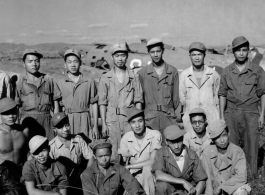 Chinese aircraft mechanics and engineers pose at an air base in China during WWII. Behind them are damaged airplanes used for parts.