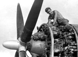 An American aircraft mechanic doing maintenance sits astride a large aircraft engine. In the CBI during WWII.