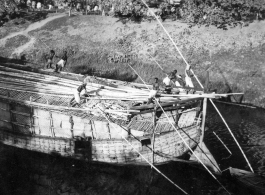 Numerous boatmen use poles to push a large boat in a waterway in India during WWII.