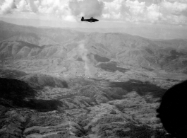 B-25 Mitchell bomber in flight in the CBI, in the area of SW China, Indochina, or Burma. Notice smoke rising in the center. During WWII.