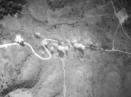 Aerial view as B-25 Mitchell bombers bomb a barren stretch of the Burma Road in 1944. Strangely no traffic is obvious on the road, so maybe this is just an attempt to slow down the enemy by damaging the road. Notice the encampment on the right.