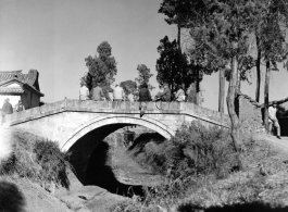 Chinese civilians and Nationalist soldiers pass the time on a small bridge in Yunnan, China, probably near Kunming or Yangkai base. During WWII.  From the collection of Hal Geer.