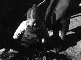 A small child plays at a charcoal hearth in China during WWII. These might be refugees at Liuzhou.