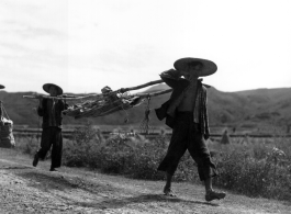 Men shoulder a stretcher, possibly carrying recovered human remains. During WWII, in China.