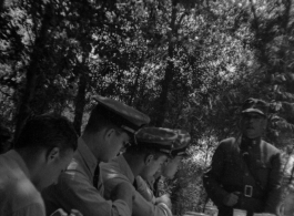 A Chinese officer makes a toast or speech as SACO members share a meal with Nationalist soldiers, in the shade of trees, during WWII. In northern China.