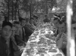 SACO members share a meal with Nationalist soldiers, in the shade of trees, during WWII. In northern China.