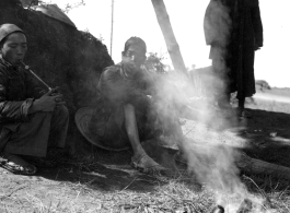 Local people in China: Men smoke and rest in the shade while their food heats over a tiny fire.