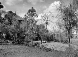 A village scene in Yunnan province, China, with ponds around a raised walkway, and an ornate building among the trees. During WWII.