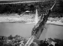 In this image, a bridge somewhere in southwest China, Indochina, or Burma, is bombed by American B-25s, running in very fast at almost tree-top level (notice the perspective of the camera, which is very close to the ground level), with bombs dropping in the river around the bridge. Three to four splash sites can be seen. The bombers come in so fast and unexpectedly that people on the bridge are caught unprepared, as in the blown up image below, where men (either workers or Japanese soldiers) can be seen fra