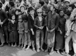 Burma Road dedication parade and ceremony in Kunming, China, on or around February 4, 1945, during WWII. Review of first convoy (or one of the first convoys) to reach China. Ranks of soldiers and civilians, waiting in anticipation of the parade, speeches, and first trucks to arrive.