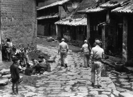 Armed GIs walk on road at Yangkai village, as villagers look up and take note. During WWII.