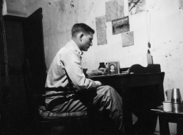 View inside barracks for two GIs in Yunnan, China, during WWII--GI at desk.