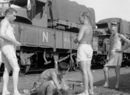 US soldiers bathing at a faucet during war, alongside a railway.