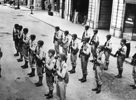 GIs, with apparent Army Air Forces shoulder patches, stand in ranks in a place that uses the word "haberdashery" (as on shop window to the right)--likely India, but also possibly Britain.