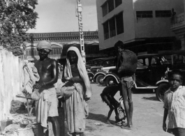 Poor people on street next to nice cars.  Scenes in India witnessed by American GIs during WWII. For many Americans of that era, with their limited experience traveling, the everyday sights and sounds overseas were new, intriguing, and photo worthy.