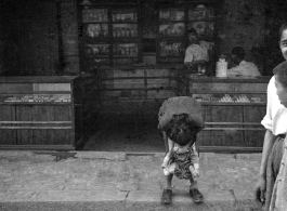 A child relieving itself streetside, in front of a shop, in China during WWII.