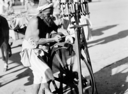 Man sharpens knives on road in town in Burma or India.  Near the 797th Engineer Forestry Company.  During WWII.