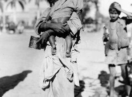 Begging woman holds child on road in town in Burma or India.  Near the 797th Engineer Forestry Company.  During WWII.