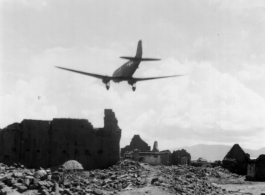 A US C-47 transport plane flies over a damaged village, probably outside of Kunming, Yunnan province.