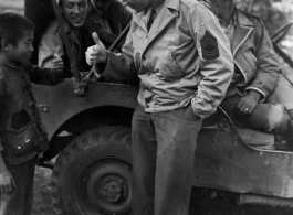 GI exchanges a thumbs up with kid in China, while other GIs observe from jeep. During WWII.