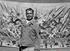 An American serviceman in the CBI, standing in front of an elaborate embroidered silk sheet, during WWII.