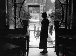 A woman stands in the doorway to a tea house or guild hall or similar meeting place. In Kunming, during WWII.
