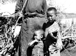 Local rural people in China: An elderly man smokes a long pipe while watching over two children.