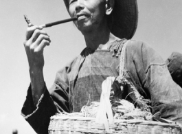 Local people in China: A farmer in the field smokes a short pipe. During WWII.