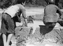 Two boys in China look at something interesting below the road they are on. During WWII.