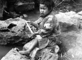 Impoverished kid sitting creekside in China during WWII.