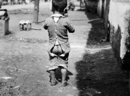Local people in China: A young child with split pants in a street in China, during WWII.