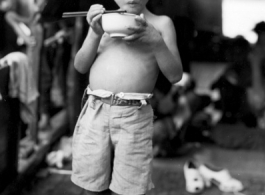 A young boy eats a meal on a boat in China during WWII, probably in Guangxi province, likely Liuzhou or Guilin.