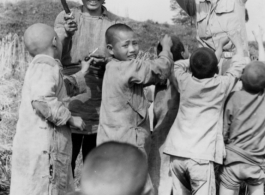 A GI hands out treats (likely candy) to enthusiastic Chinese kids as a farming woman smiles. During WWII.