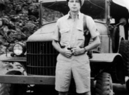 A GI stands in front on a truck on a road in the CBI during WWII.