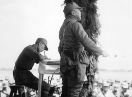 Chinese offiGen. Wei Lihuang (卫立煌) gives speech to assembled troops, and another person makes notations on a paper, on stage during rally.er gives speech during exercises in southern China, probably Yunnan province, or possibly in Burma.