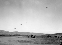 Several P-40 fighters pass over the runway and begin a "break out" to land at Yangkai, Yunnan province. American B-25H bomber are visible in the foreground of this picture taken in the CBI.