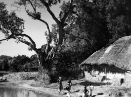 Women collect water from pond in front of house with thatched roof.  Scenes in India witnessed by American GIs during WWII. For many Americans of that era, with their limited experience traveling, the everyday sights and sounds overseas were new, intriguing, and photo worthy.