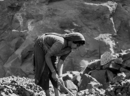 Woman crushes rock by hand, for use in construction.  Scenes in India witnessed by American GIs during WWII. For many Americans of that era, with their limited experience traveling, the everyday sights and sounds overseas were new, intriguing, and photo worthy.